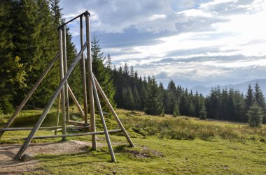 Ağaçlar, çim tarlaları ve sakin gökyüzünün altındaki uzak dağ manzaralarıyla çevrili orman açıklıklarında kırsal ahşap salıncaklar. Doğal ve açık hava eğlencesini karıştıran sakin bir yer. Karpatlar, Ukrayna