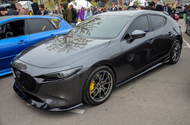 Gösterişli, koyu gri modifiye Mazda 3 hatchback araba fuarında. Özel yapım çok dilli tekerlekler, sarı fren ayarları ve agresif ön dudak spikeri var.