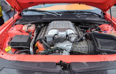 Turuncu Dodge Challenger 'daki güçlü Hemi motorunun ayrıntılı görüntüsü, karmaşık mekanik bileşenlerini ve açık kaputu gösteriyor.