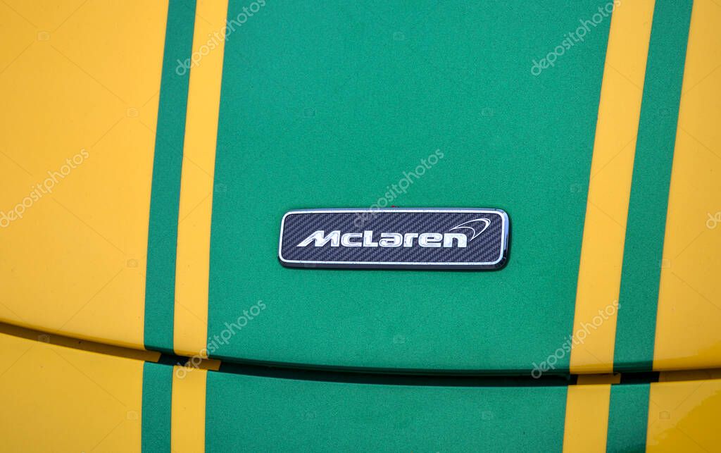 Close-up of a McLaren logo on a vibrant yellow car with green racing stripes. The emblem is sleek, indicating high-performance automotive design and branding