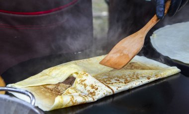 Lezzetli krepler ustalıkla katlanıp bir şef tarafından ısıtılmış ızgarada pişiriliyor. Sıcak buhar ve altın tabakalar, yeni hazırlanmış sokak yemeklerinin işçiliğini ve sıcaklığını ön plana çıkarıyor.