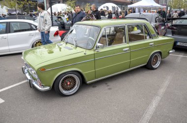 Eski zeytin yeşili Lada 2103 sedan klasik Sovyet dönemi araç tarihi tasarım ve ince modern özelleştirme karışımı sergiliyor.