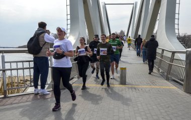 Maraton koşucuları açık gökyüzünün altındaki bir yarışta enerji ve kararlılıklarını sergileyerek köprüden geçiyorlar.