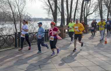Aktif bireyler, açık ve güneşli gökyüzü altında, doğal park yolu boyunca birlikte koşuyorlar, yoldaşlığın ve uygunluğun tadını çıkarıyorlar.