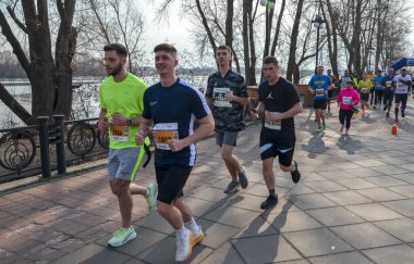 Aktif bireyler, açık ve güneşli gökyüzü altında, doğal park yolu boyunca birlikte koşuyorlar, yoldaşlığın ve uygunluğun tadını çıkarıyorlar.