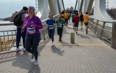 Maraton koşucuları açık gökyüzünün altındaki bir yarışta enerji ve kararlılıklarını sergileyerek köprüden geçiyorlar.