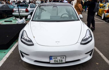 Minimalist tasarımı ve panoramik cam çatılı beyaz Tesla Model 3 elektrikli araba. Modern estetik ve elektrik güç treni onu herhangi bir otomotiv olayında ön plana çıkarıyor.