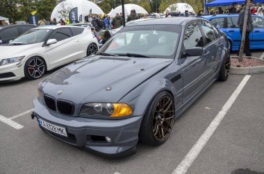 Bir mat gri BMW E46 sedan, geniş gövde kiti ile ağır modifiye, düşük süspansiyon ve bronz çok dilli tekerlekler, açık havada park edilir