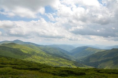 Parça parça bulutlu bir gökyüzünün altında ufuk boyunca yayılmış çalı ve otlakların karışımından oluşan tepeler, dinginliği ve doğal güzelliği somutlaştırıyor. Svydovets, Karpatlar, Ukrayna