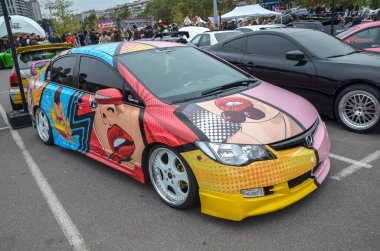 Canlı özelleştirilmiş Honda Civic sedan. Çizgi roman grafikleri, parlak renkler ve iki farklı yarı açık havada sergileniyor.