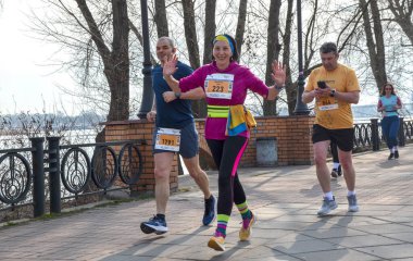 Güneşli yollarda düzenlenmiş açık hava maratonuna katılan bir grup koşucu manzaralı, spor atmosferi, dostluk ve atletizm hedefleri yaratıyor.