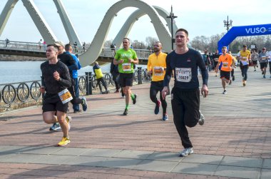 Bir köprünün yakınındaki nehir kenarındaki yolda yarışan enerjik bireyler grubu