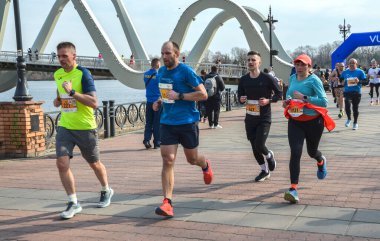 Bir köprünün yakınındaki nehir kenarındaki yolda yarışan enerjik bireyler grubu