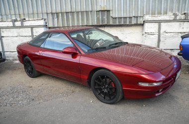 Kırmızı Ford Probe iki kapılı otomobil, belirgin ön far ve aerodinamik tasarımı ile tanınıyor, Amerikan ve Japon otomotiv mühendisliğinin bir karışımını temsil ediyor.