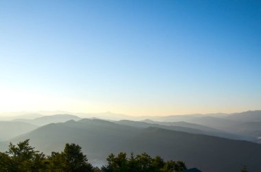 Güneş doğarken altın bir gökyüzünün altındaki katmanlı dağ manzarası sükunet ve doğal güzelliği gözler önüne seriyor. Karpat Dağları, Ukrayna