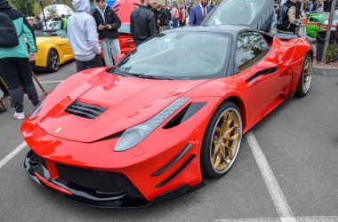 Kapsamlı siyah aerodinamik modifikasyonları ve çarpan altın rengi çoklu tekerlekleri olan özel kırmızı Ferrari 458 Italia Prior Design açık hava araba fuarında sergilenmektedir.