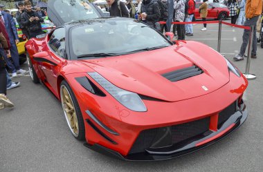 Kapsamlı siyah aerodinamik modifikasyonları ve çarpan altın rengi çoklu tekerlekleri olan özel kırmızı Ferrari 458 Italia Prior Design açık hava araba fuarında sergilenmektedir.