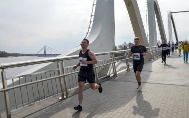 Koşucular çağdaş bir köprüyü geçerken bir maraton etkinliğine katılıyorlar, çabalarını, odaklanmalarını ve atletizmini sergiliyorlar.