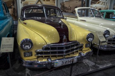 Çarpıcı iki tonlu klasik araba, GAZ-12 ZIM, krem gövde ve koyu bordo kaplama çizgili, belirgin krom ızgara ve tampon, kapalı alanda sergileniyor.