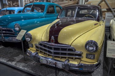 Çarpıcı iki tonlu klasik araba, GAZ-12 ZIM, krem gövde ve koyu bordo kaplama çizgili, belirgin krom ızgara ve tampon, kapalı alanda sergileniyor.