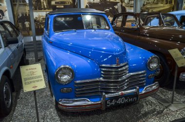 Klasik, parlak mavi GAZ-M20 Pobeda belirgin krom ızgara ve farlar, diğer klasik arabalarla birlikte kapalı alanda sergileniyor 
