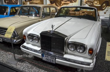 Beyaz, 1990 model, üstü açık Rolls-Royce Corniche, ikonik krom ızgarası, Ecstasy amblemi ve lüks bronz deri iç mekanı.