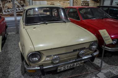 Krem renkli Skoda 100 devrimci arka motor, arkadan çekişli sedan, ayırt edici ızgara ve dairesel farlar içeriyor.