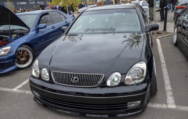 Pürüzsüz tasarımı ve açık hava araba fuarında park etme potansiyeliyle tanınan ağır modifiye edilmiş siyah Lexus sedan.