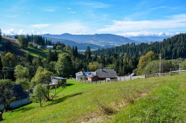Büyüleyici kırsal köy, yemyeşil çayırlarda ormanlık tepeler ve uzak dağlarla örülü. Resim, huzurlu, resimli kırsal yaşamı ve doğal güzelliği tasvir ediyor. Karpatlar, Ukrayna