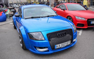 Geniş çamurlukları, büyük, siyah ızgarası ve açıkta bırakılmış soğutucu boruları olan agresif geniş gövde kiti ile mavi Audi TT, önemli performans değişikliklerini gösteriyor. 