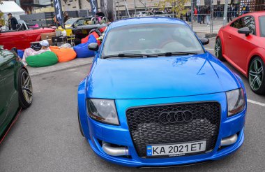 Geniş çamurlukları, büyük, siyah ızgarası ve açıkta bırakılmış soğutucu boruları olan agresif geniş gövde kiti ile mavi Audi TT, önemli performans değişikliklerini gösteriyor. 