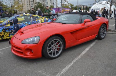 Üstü açılır kırmızı Dodge Viper, belirgin yan egzozu, uzun hava delikli kaputu ve siyah yumuşak üstü olan ikonik kas ve agresif stiline sahiptir.