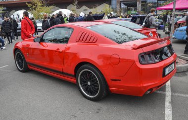 Canlı kırmızı Ford Mustang coupe, kırmızı gövdeye spor kontrastı sağlayan, parlak dudak siyah yan etekleri ve siyah ayna kapakları ile siyah çoklu konuşan tekerlekler içerir.