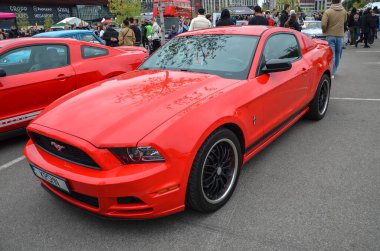 Canlı kırmızı Ford Mustang coupe, kırmızı gövdeye spor kontrastı sağlayan, parlak dudak siyah yan etekleri ve siyah ayna kapakları ile siyah çoklu konuşan tekerlekler içerir.