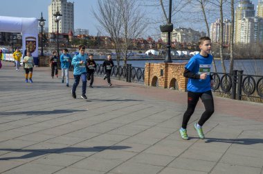 Nehir kenarındaki manzaralı bir gezinti alanında yarışan bir grup çocuk enerjiyi, sporu ve toplumu ön plana çıkarıyor.