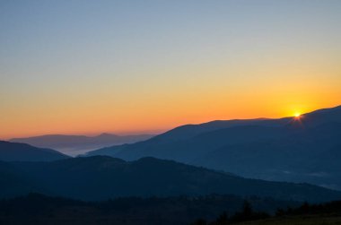 Sabah güneşi, koyu mavi dağların görkemli aralığında sıcak renkler saçar ve ufukta sıcak bir parıltı bırakır. Karpatlar, Ukrayna