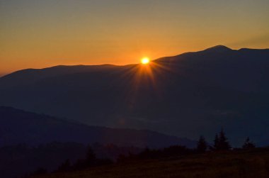 Sabah güneşi, koyu mavi dağların görkemli aralığında sıcak renkler saçar ve ufukta sıcak bir parıltı bırakır. Karpatlar, Ukrayna