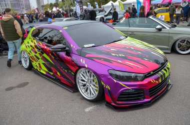 Modifiye edilmiş mor ve neon yeşil Volkswagen Scirocco açık hava araba fuarında sergileniyor. Sivri çizgileri olan özel ambalajlı araç özellikleri indirilmiş süspansiyon ve büyük çoklu konuşma tekerlekleri