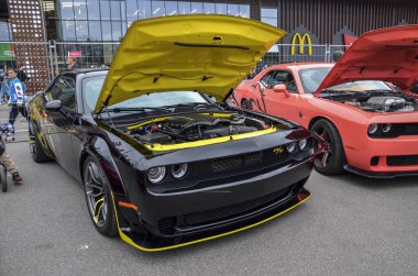Siyah modern Dodge Challenger RT, agresif duruşu, geniş gövdeli çamurlukları, açık kaputu, öne çıkan sarı aksanlı süper şarjlı motoru ortaya çıkarıyor.