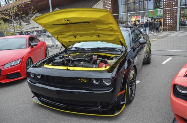 Siyah modern Dodge Challenger RT, agresif duruşu, geniş gövdeli çamurlukları, açık kaputu, öne çıkan sarı aksanlı süper şarjlı motoru ortaya çıkarıyor.