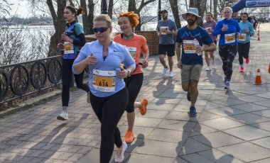 Bir maraton koşan bir grup, güneşli bir günde, açık havada güneşli bir nehir kenarında egzersiz yapıyor, zindelik, dayanıklılık ve sağlıklı bir yaşam tarzı sergiliyor. 