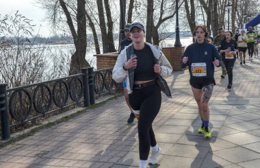 Bir maraton koşan bir grup, güneşli bir günde, açık havada güneşli bir nehir kenarında egzersiz yapıyor, zindelik, dayanıklılık ve sağlıklı bir yaşam tarzı sergiliyor. 