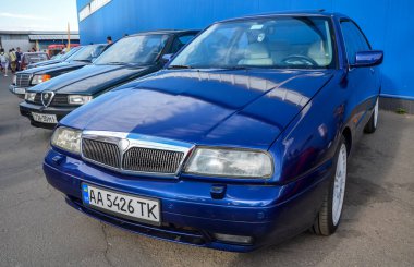 Mavi 1997 Lancia Kappa sedan, o dönemin Lancia modellerinin gelişmiş, az gösterilen tasarım özelliklerini sergiliyor, kendine özgü ızgaraları ve açık farları var.