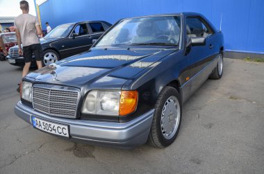 Siyah 1995 Mercedes Benz W124 coupe klasik Mercedes-Benz ızgarası ve büyük farlarıyla zarif, sütunsuz coupe tasarımı sergiliyor.