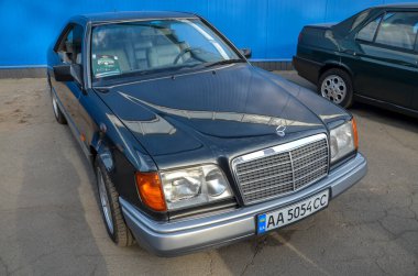 Siyah 1995 Mercedes Benz W124 coupe klasik Mercedes-Benz ızgarası ve büyük farlarıyla zarif, sütunsuz coupe tasarımı sergiliyor.