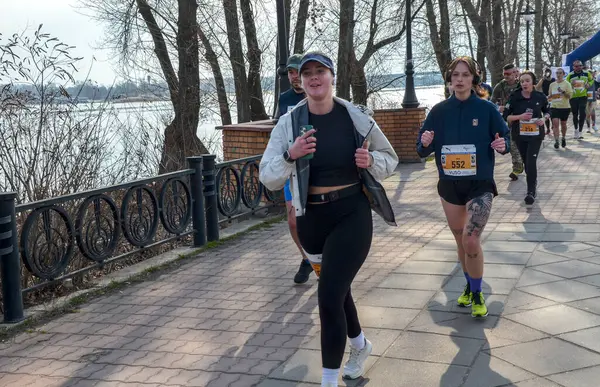 Bir maraton koşan bir grup, güneşli bir günde, açık havada güneşli bir nehir kenarında egzersiz yapıyor, zindelik, dayanıklılık ve sağlıklı bir yaşam tarzı sergiliyor. 