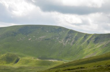 Scenic view of verdant rolling hills enveloped in lush green vegetation, accentuated by a partly cloudy skies subtle contrast, evoking a serene and tranquil natural atmosphere. Carpathian Mountains