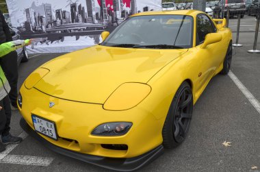 Parlak sarı Mazda RX-7. Pürüzsüz, aerodinamik tasarlanmış, kendine özgü döner motoruyla ünlü hafif bir spor araba.