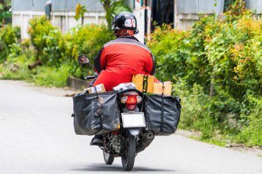Bangkok, Tayland - 05 Ağustos 2022: Kimliği belirsiz kırmızı üniformalı teslimatçı motosikletle Bangkok, Tayland 'a bir paket getirdi.