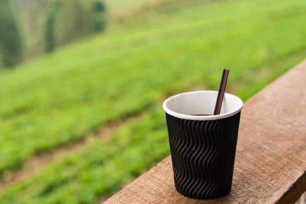 Paper cup of coffee with sunrise on green field background.